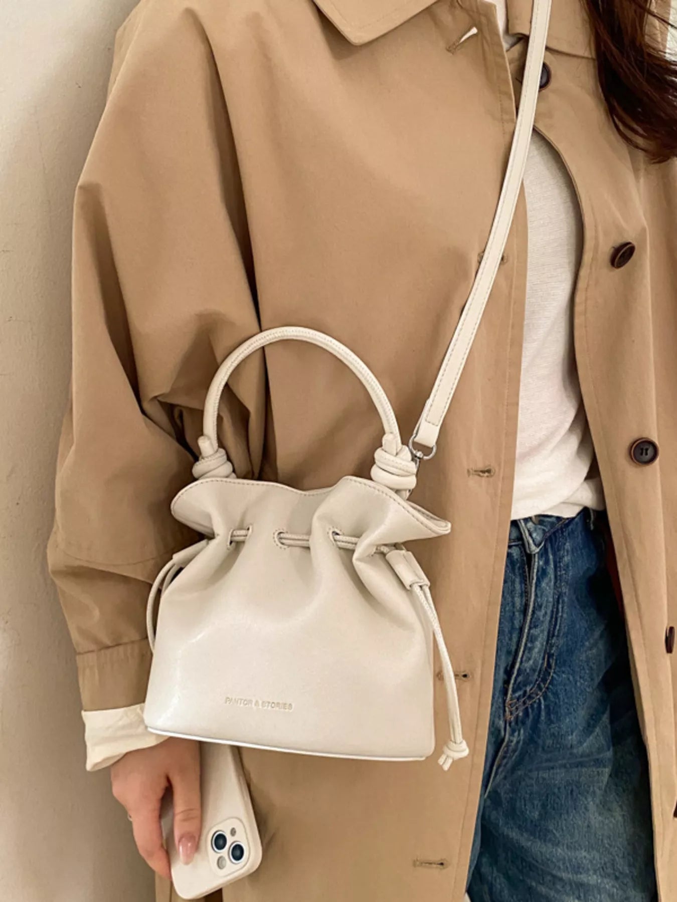 Person wearing a beige trench coat holding a white drawstring bag.
