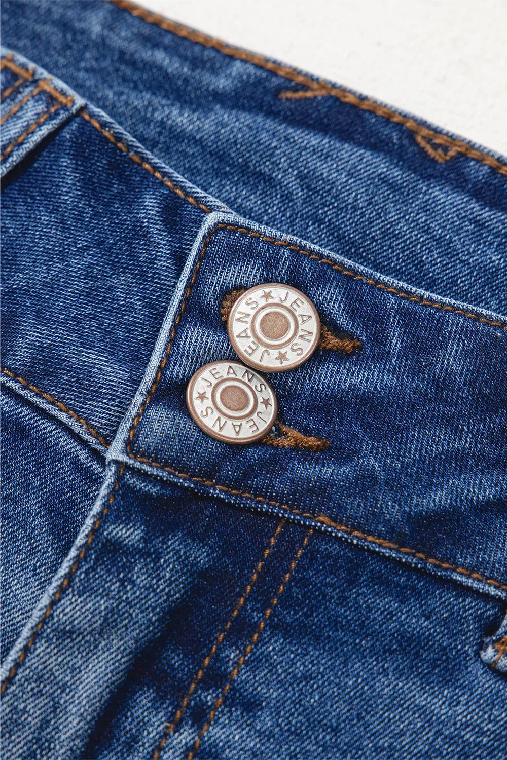 Close-up of blue denim fabric with metal buttons on a white background