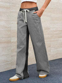 Person wearing gray checkered pants with a white drawstring against a beige wall.