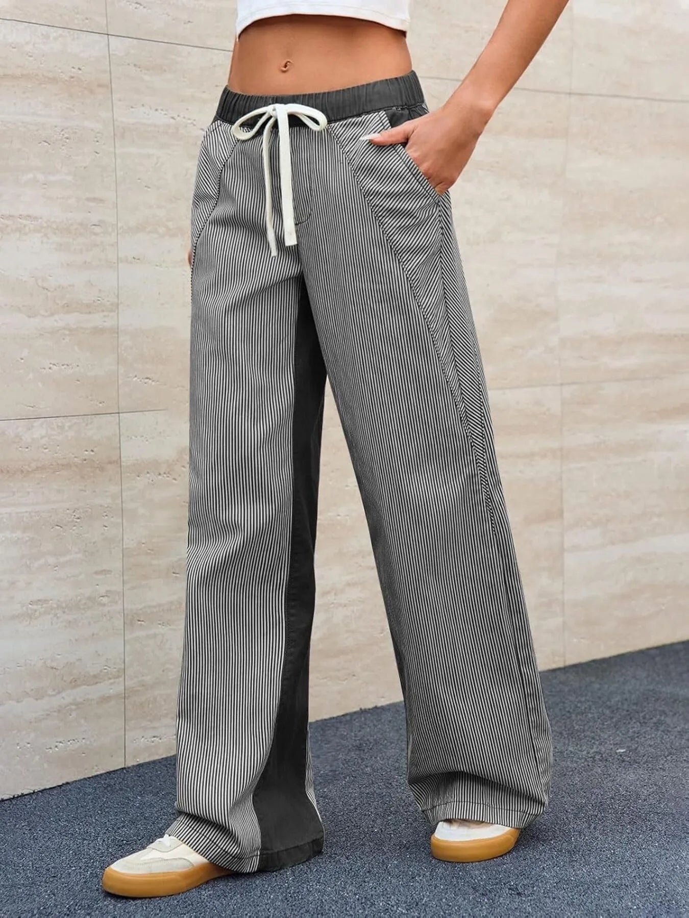 Person wearing gray checkered pants with a white drawstring against a beige wall.