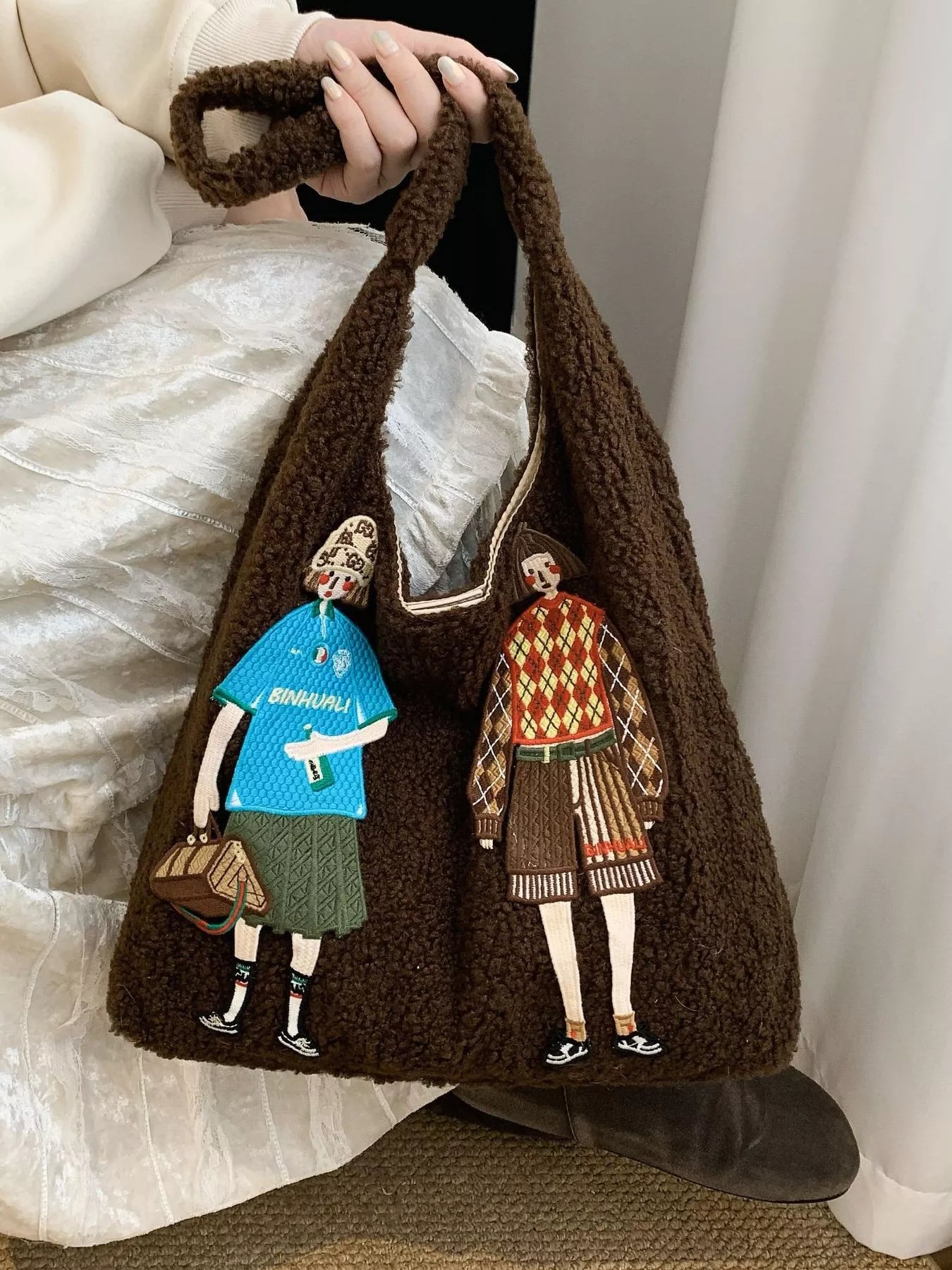 Brown textured bag with embroidered figures of a man and a woman holding hands.