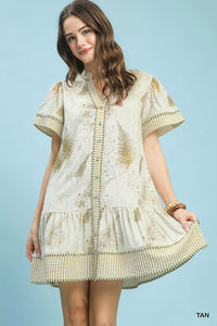 Woman wearing a beige and white embroidered dress against a light blue background