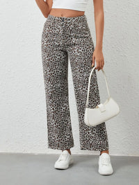 Person wearing leopard print pants and white sneakers holding a white handbag against a plain background
