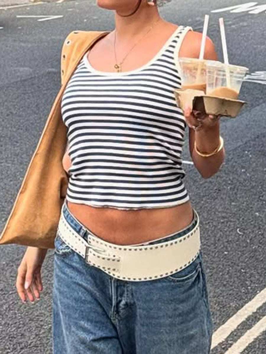 Person wearing a striped tank top and blue jeans, holding a drink, on a street.