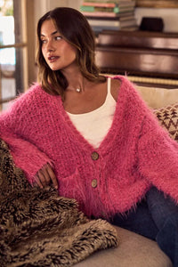 Woman wearing a pink cardigan sitting on a couch in a cozy living room.
