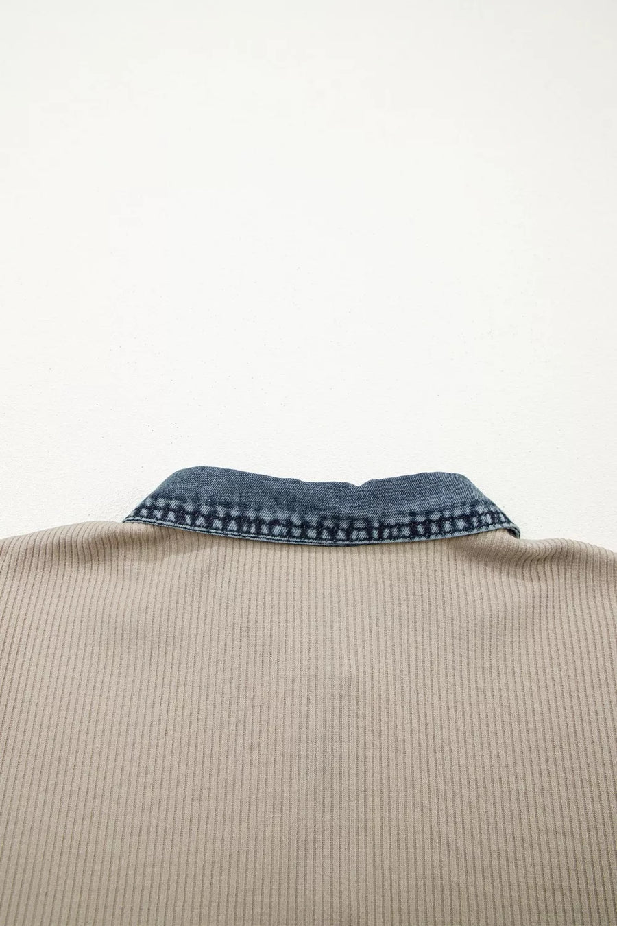 Close-up of a beige garment with a blue denim collar on a white background
