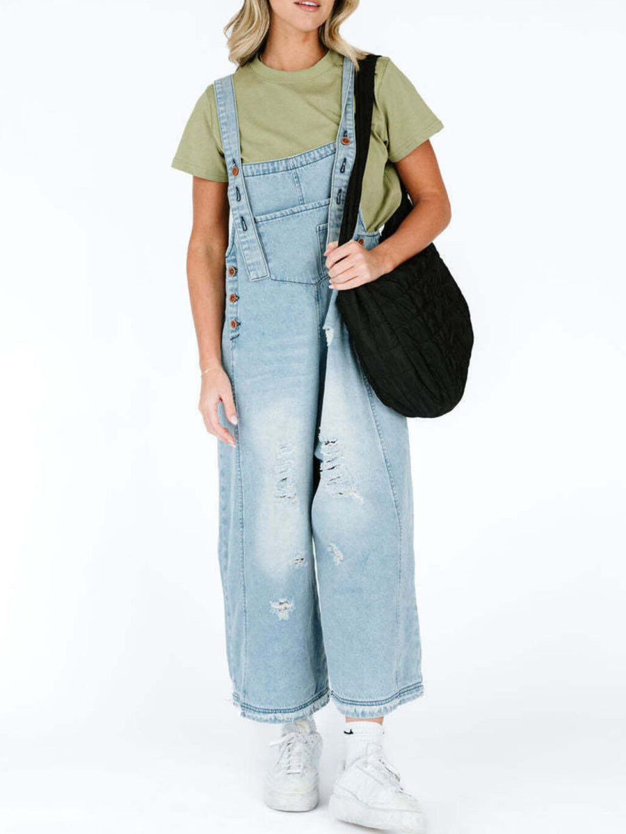 Person wearing light blue denim overalls with a black bag on a white background