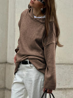 Person wearing a brown sweater and white pants against a light-colored wall.