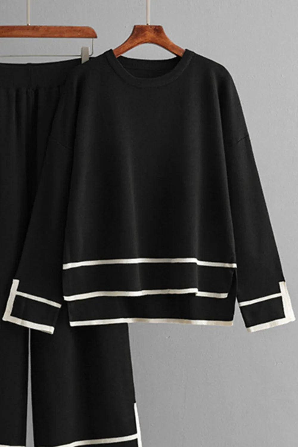 Black outfit with white trim on a hanger against a gray background