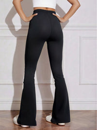 Person wearing black flared pants against a white wall