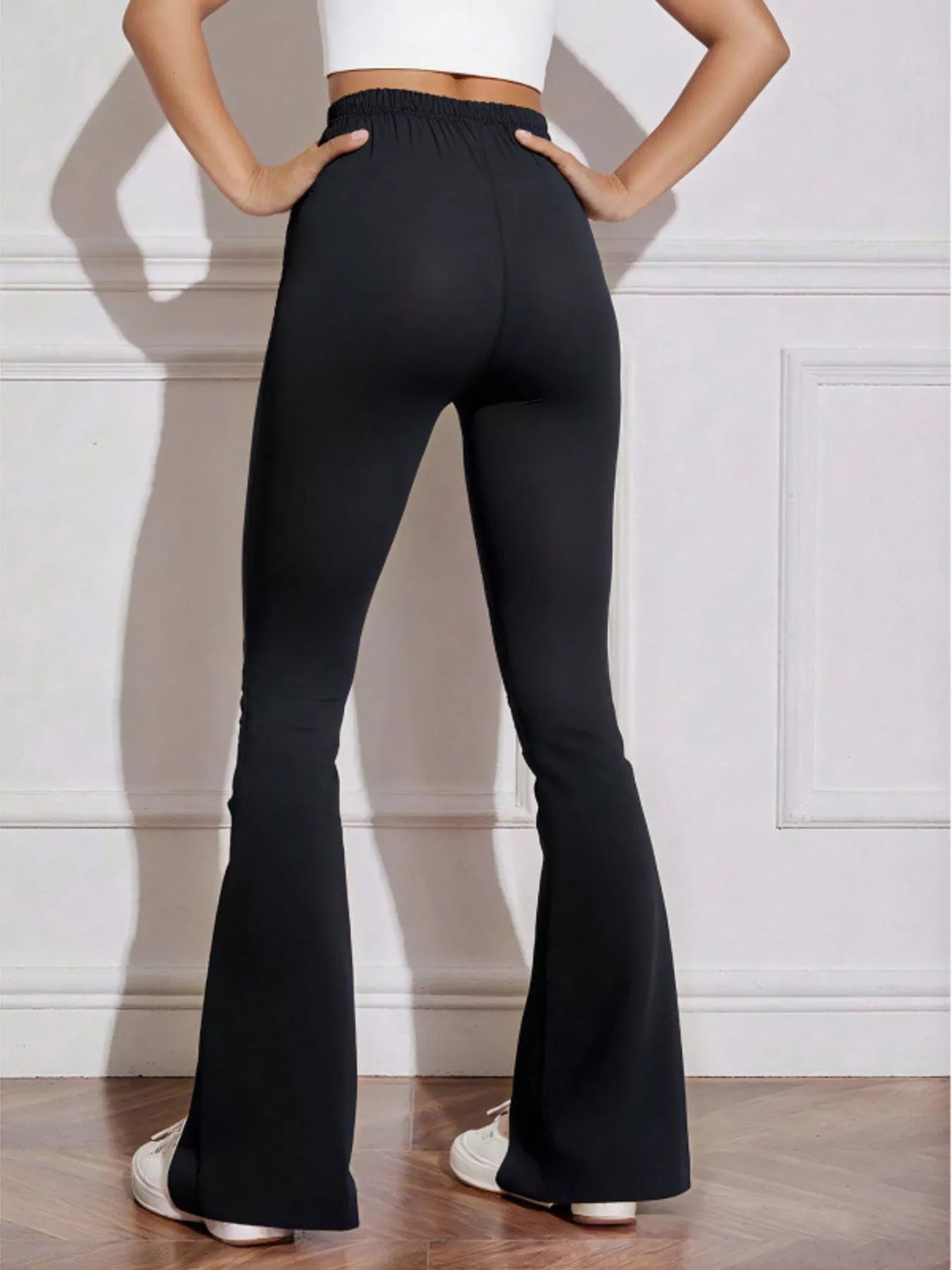 Person wearing black flared pants against a white wall