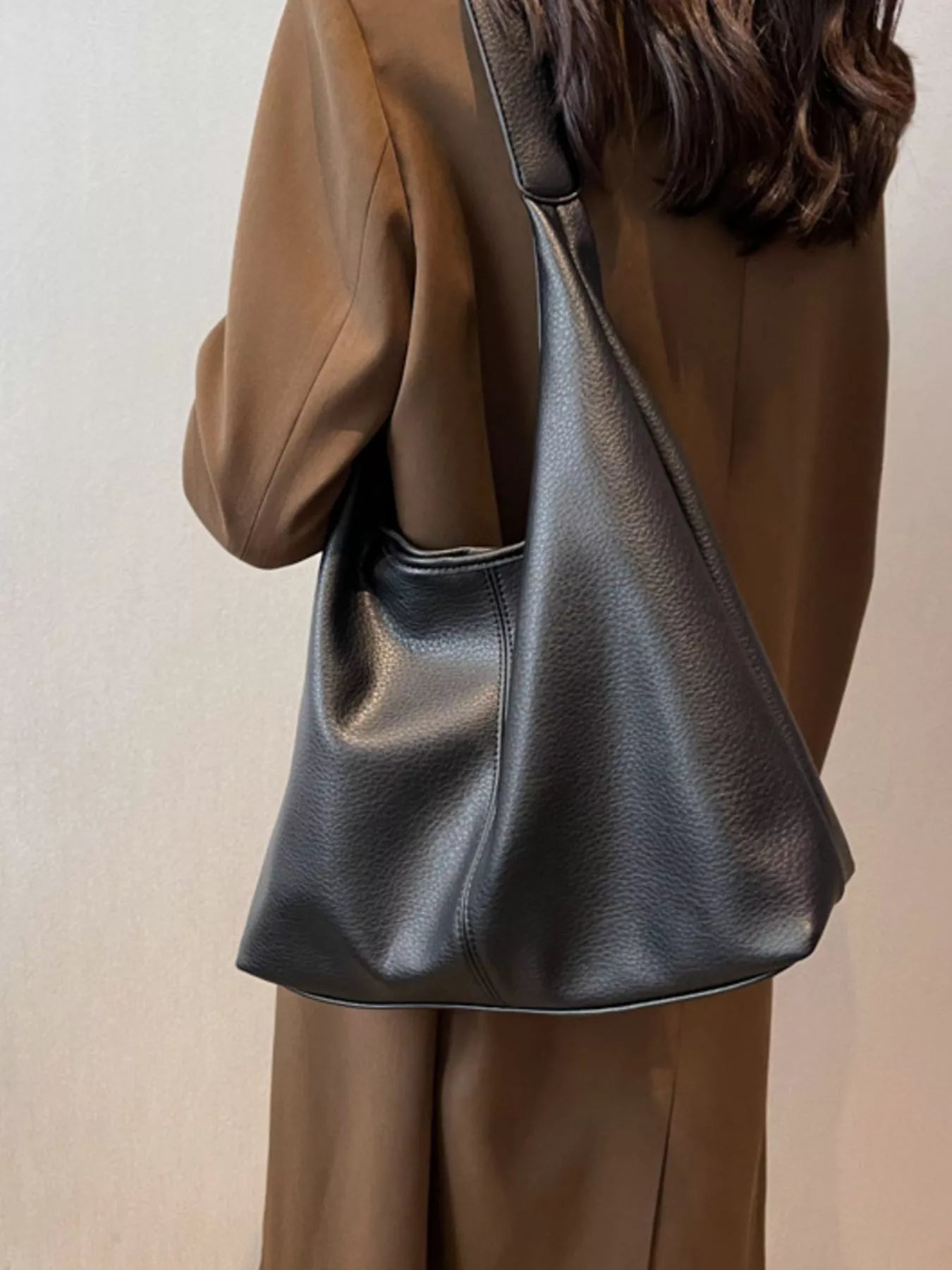 Person wearing a brown coat with a black leather handbag on a plain background