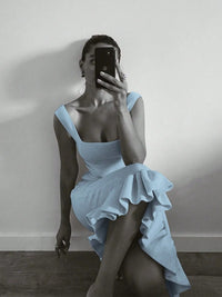 Person wearing a light blue dress with ruffled details, sitting against a plain wall.