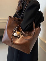 Brown leather tote bag with decorative keychain held by a person wearing a black coat.