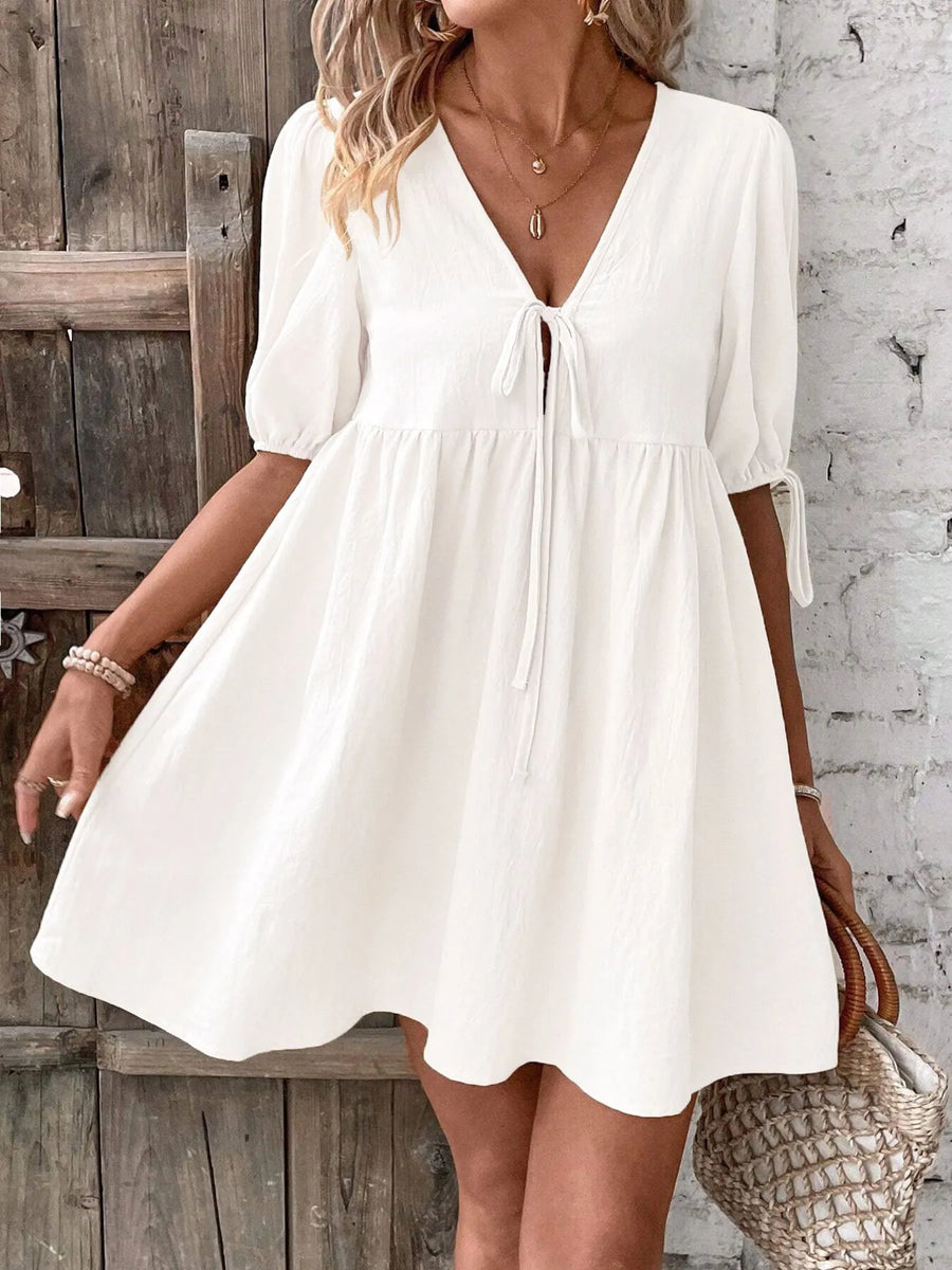 Woman wearing a white dress against a rustic wooden and stone wall.
