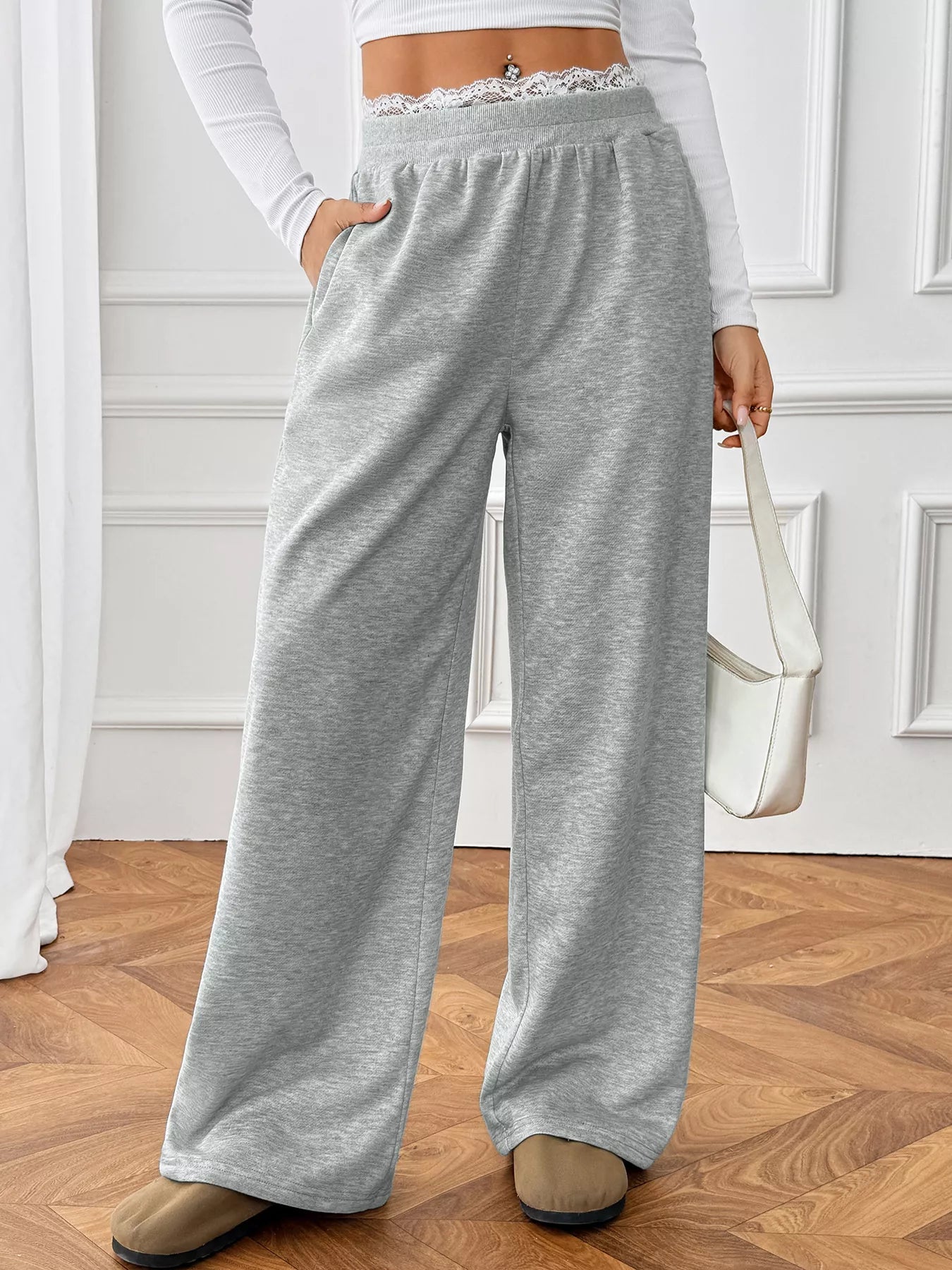 Person wearing gray sweatpants in a room with wooden flooring and white walls.