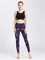Woman wearing a black sports bra and purple butterfly-patterned leggings on a white background