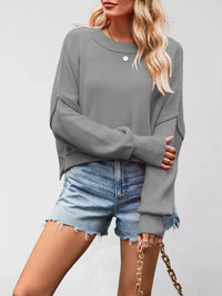 Person wearing a gray sweater and denim shorts on a plain background