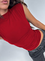 Person wearing a red sleeveless top and gray pants on a white background