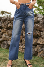 Person wearing blue jeans with slight distressing against a stone wall background