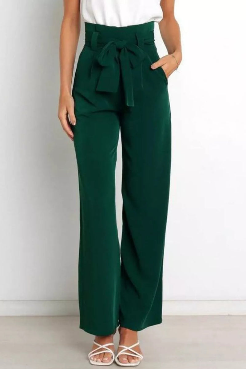 Person wearing green wide-leg pants with a white top on a plain background
