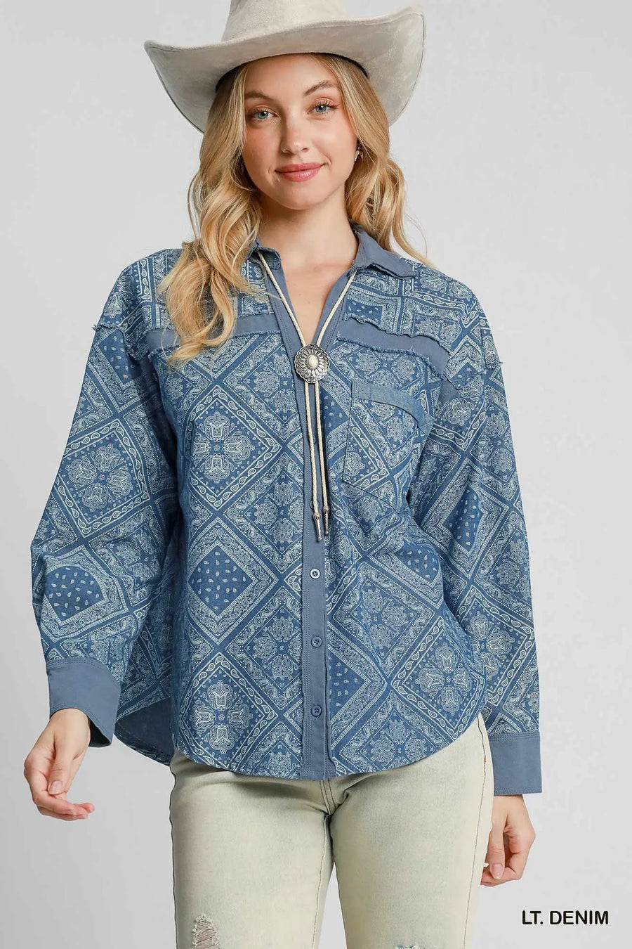 Woman wearing a blue patterned shirt with a silver tassel and a white cowboy hat on a gray background