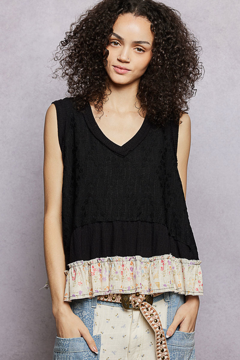 Woman wearing a black sleeveless top with ruffled trim against a gray background