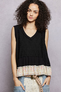 Woman wearing a black sleeveless top with ruffled trim against a gray background