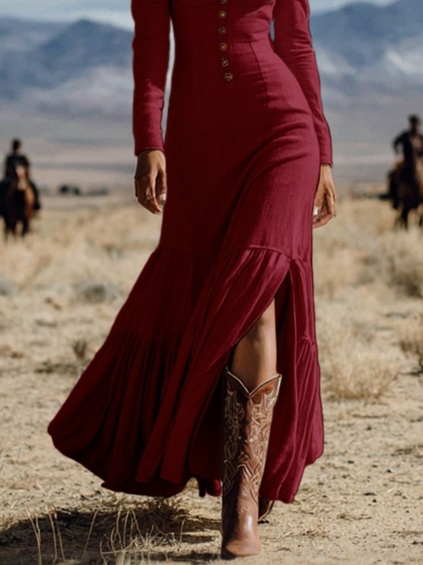 Person wearing a long burgundy dress and brown cowboy boots in a desert setting with mountains in the background.