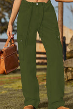 Person wearing green cargo pants holding a brown leather bag outdoors.