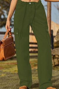 Person wearing green cargo pants holding a brown leather bag outdoors.