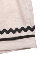 Close-up of a beige garment with black wavy trim on a white background
