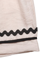 Close-up of a beige garment with black wavy trim on a white background
