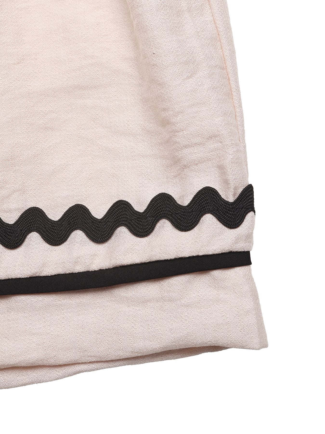 Close-up of a beige garment with black wavy trim on a white background