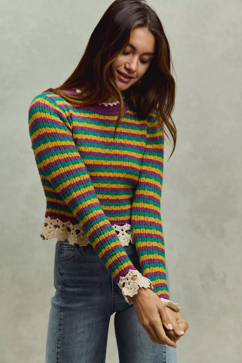 Woman wearing a colorful striped sweater with lace cuffs against a neutral background