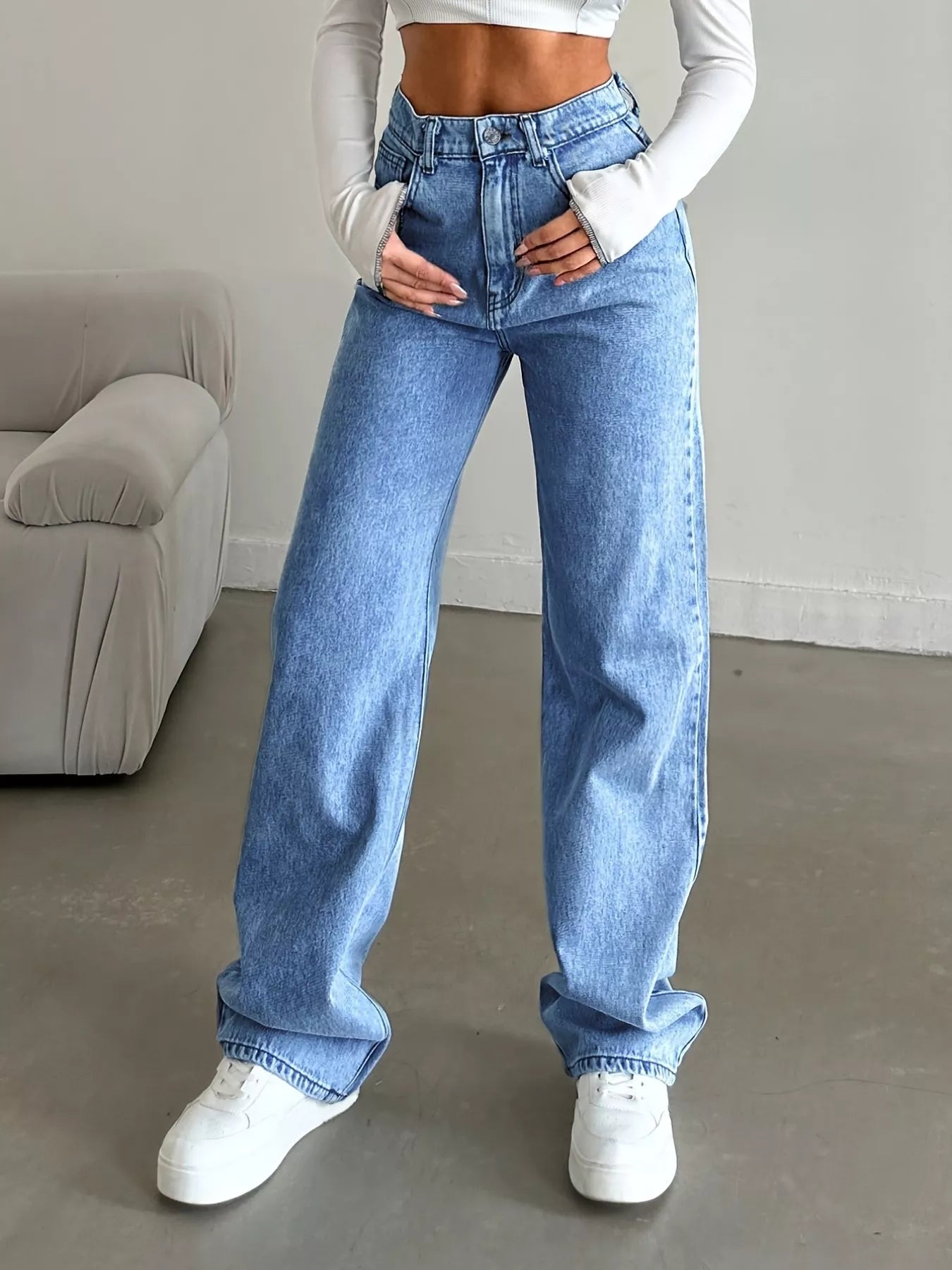 Person wearing blue jeans and white sneakers in a minimal indoor setting