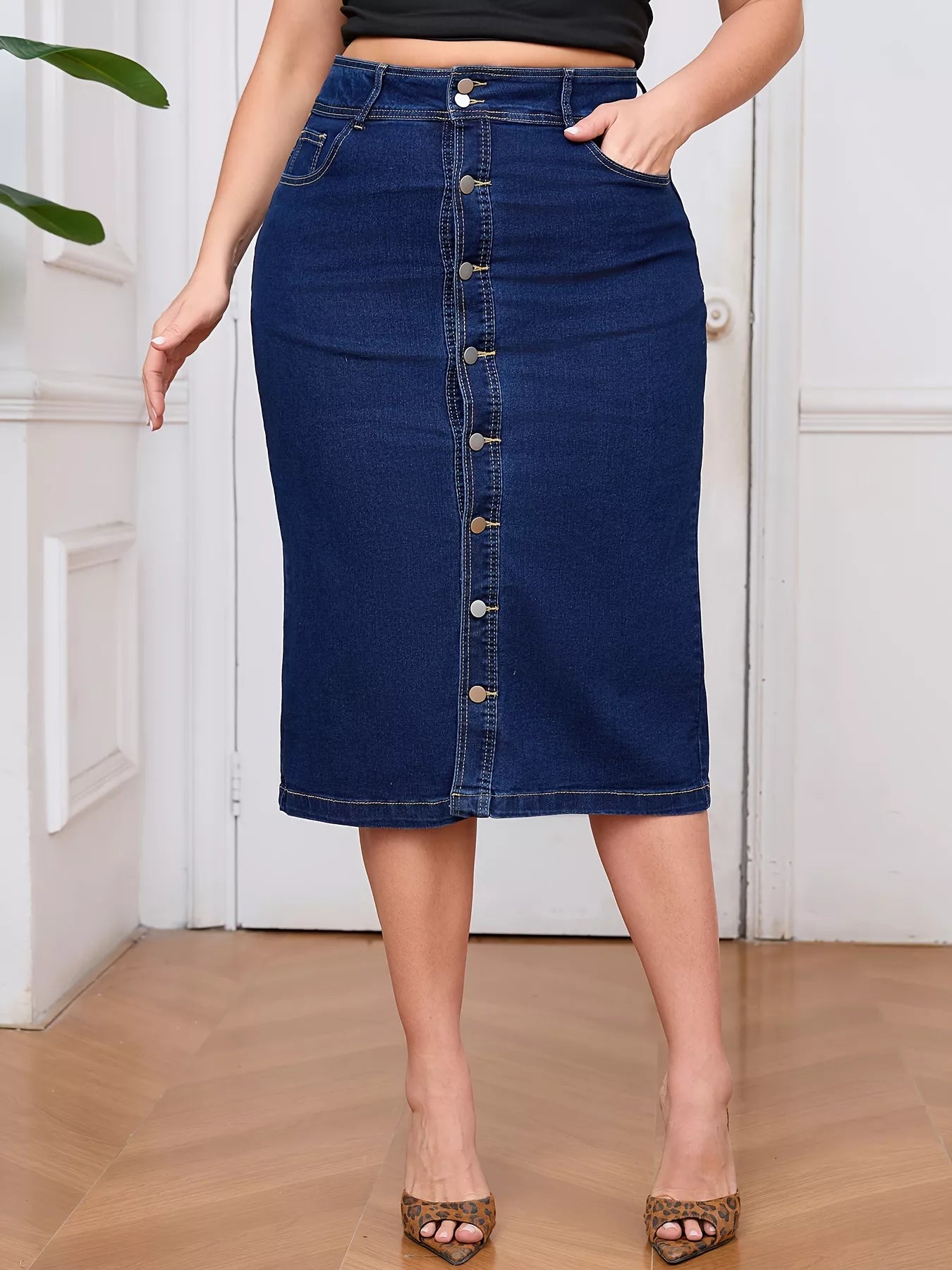 Person wearing a blue denim skirt with button details on a wooden floor.