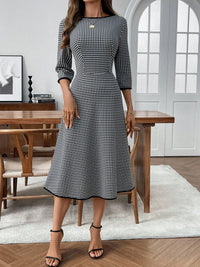 Woman wearing a black and white checkered dress in a room with wooden furniture and a large window.