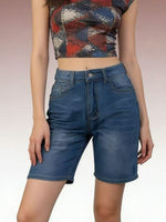 Person wearing a patterned crop top and blue denim shorts on a plain background