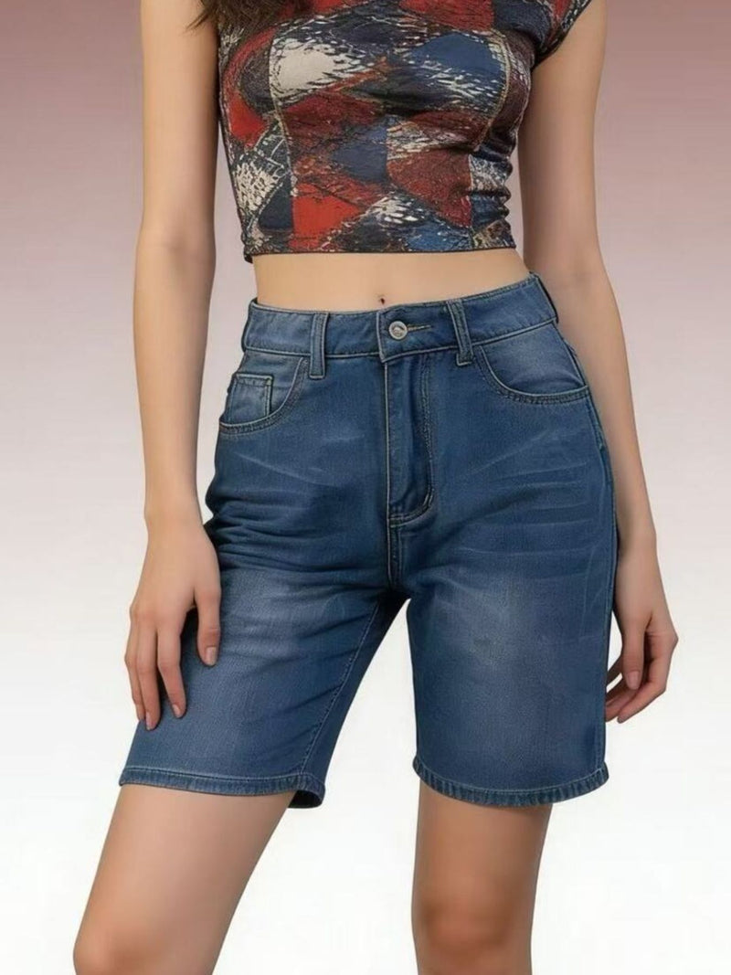 Person wearing a patterned crop top and blue denim shorts on a plain background