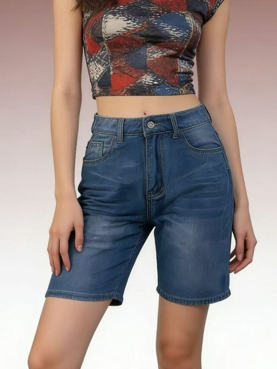 Person wearing a patterned crop top and blue denim shorts on a plain background