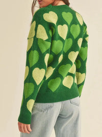 Green sweater with heart pattern worn by a person on a beige background