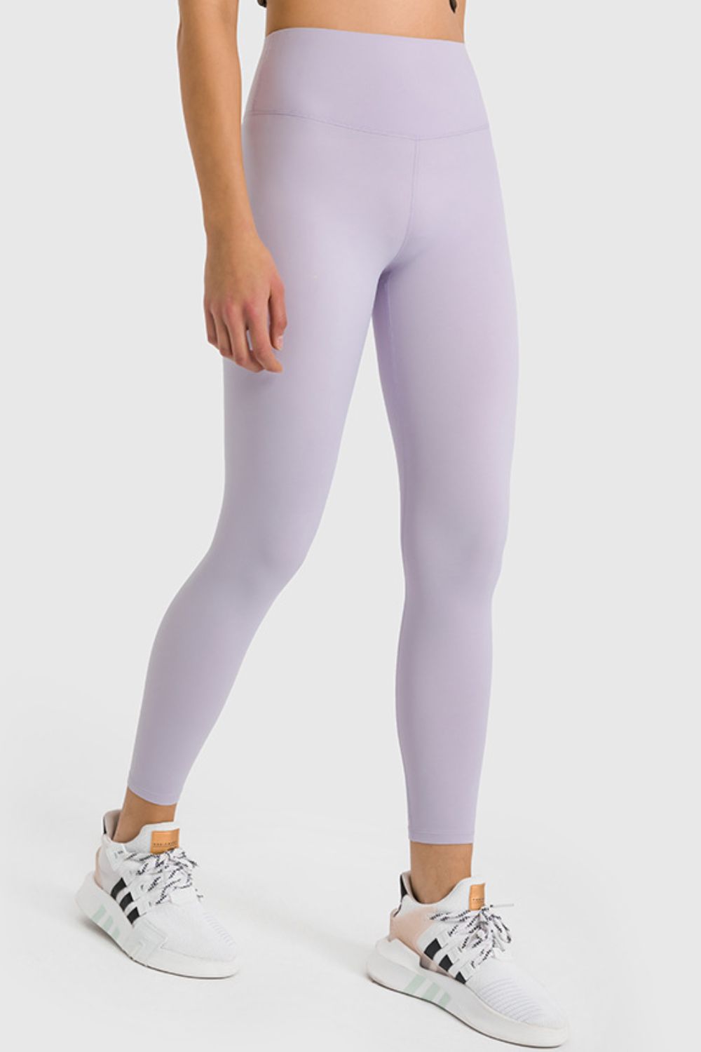 Person wearing lavender leggings with white sneakers on a light gray background