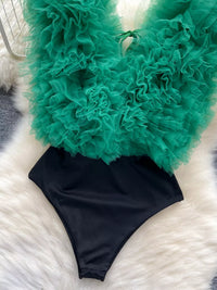 Black swimsuit with green ruffled cover-up on a white and gray patterned surface