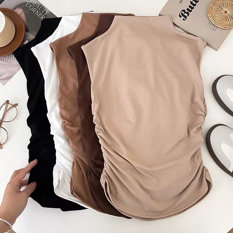 Three sleeveless tops in black, brown, and beige on a white surface with a hand pointing to the beige top.