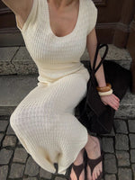 Person wearing a white ribbed dress sitting on a stone step.