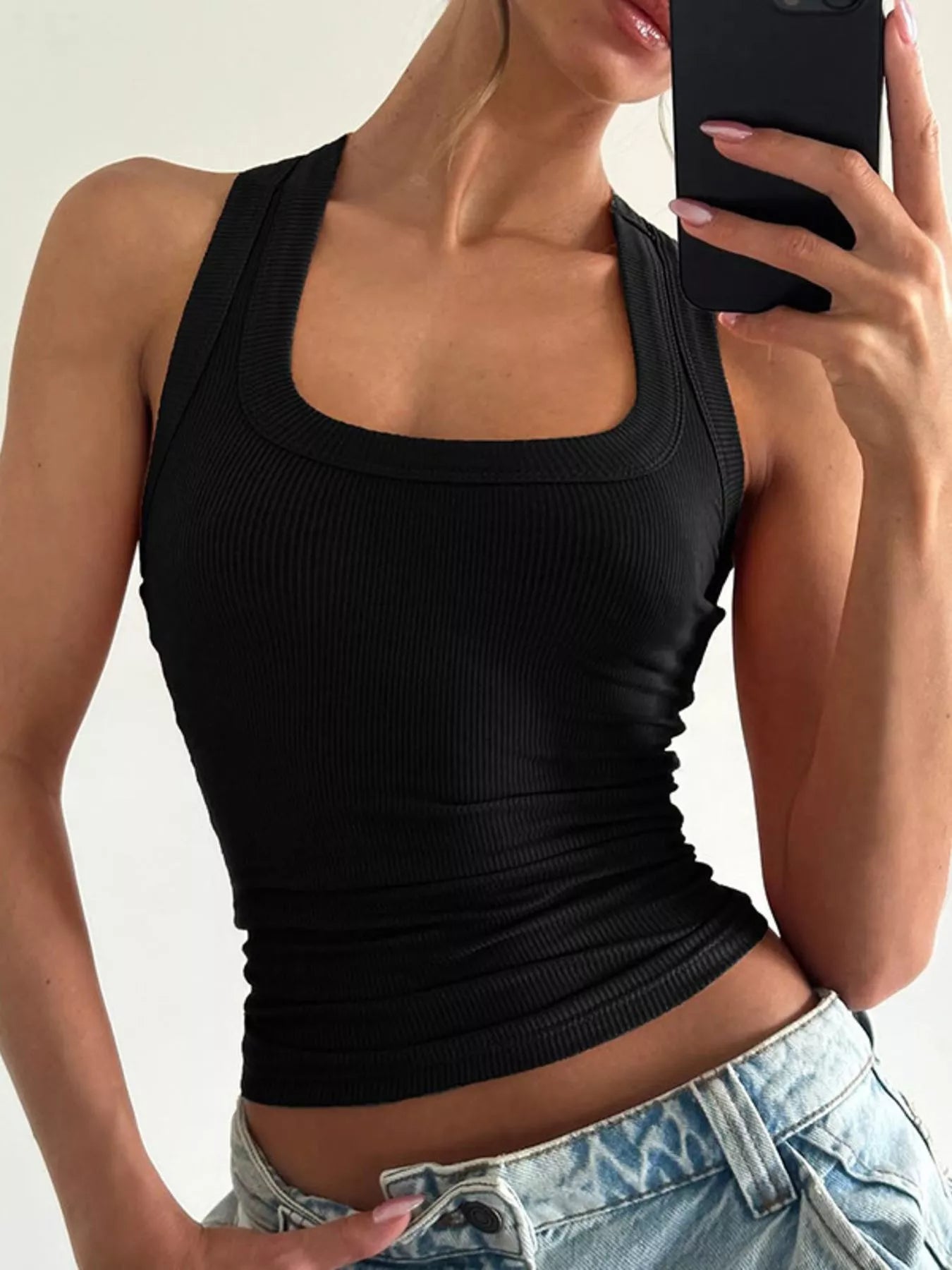 Person wearing a black tank top and blue jeans against a neutral background