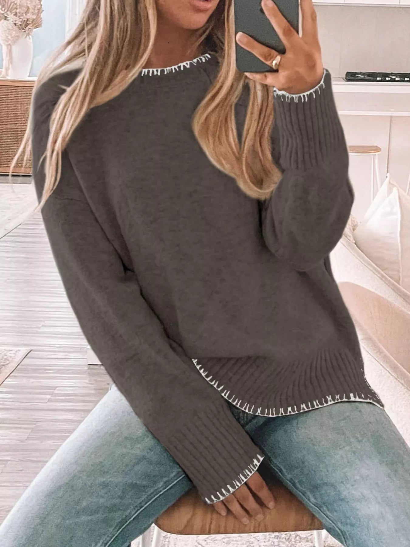 Person wearing a dark gray sweater with white trim sitting on a couch.