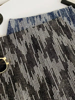 Close-up of a textured black and gray patterned rug with sunglasses on top.