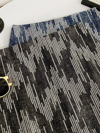 Close-up of a textured black and gray patterned rug with sunglasses on top.